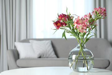 Vase with beautiful alstroemeria flowers on table in living room, space for text. Stylish element of interior design