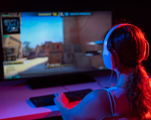 Rear view of a caucasian woman playing a computer game in neon light in the dark.