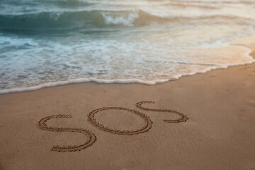 Fototapeta na wymiar SOS message drawn on sandy beach near sea