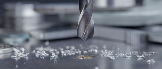 metal drill bit make holes in steel billet on industrial drilling machine with shavings. Metal work...