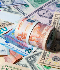 A bundle of Russian paper money in denominations of 1 and 5 thousand rubles, rolled up, lies over USA and European paper money - USD and EUR.