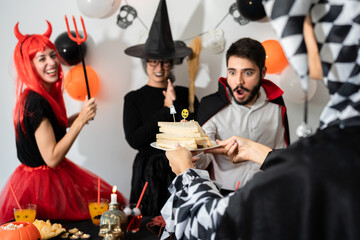 Halloween party at home. Harlequin offering sanwiches to their friends, dracula, devil and witch