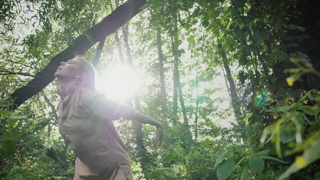 Elegant caucasian girl in a rustic dress performs a mysterious dance improvisation in a lush tropical forest nearby. Young girl enjoys nature, rests freely and dances in the forest. Dance with nature.