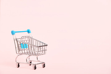 Empty shopping cart with light blue details on a pastel pink background. Minimalist design with copy space. Concepts: market deals, seasonal sales and discounts, black friday.