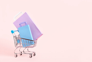 Shopping cart with purple, lilac and blue paper bags on a pastel pink background. Bright minimalist design with copy space. Concepts: market deals, seasonal discounts and rebates, black friday sales.