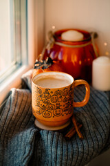 Coffee cup with autumn fall home decorations on knitted scarf on windowsill. Cozy home interior decor, Thanksgiving, Halloween concept.