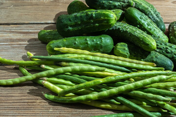 Green farm vegetables cowpea beans and cucumbers on a dark wooden background.
