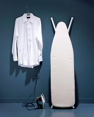 Iron near a shirt on a hanger and an ironing board