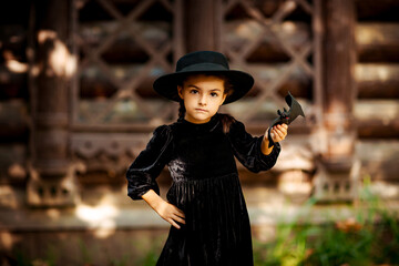 a little girl, in a black dress and hat,stands in the park and holds a bat in her hands, on...