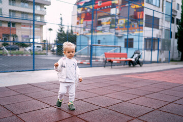 Little girl with a ponytail walks in the playground near an apartment building. High quality photo