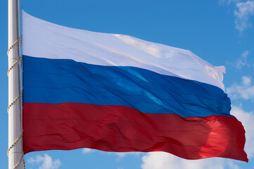 Large Russian flag against the blue sky with clouds close-up. State symbol of the Russian Federation in the wind. The flag is fixed on the highest flagpole in Russia in the city of Blagoveshchensk