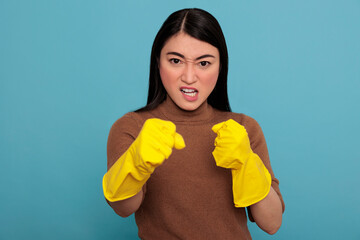 Angry aggressive asian housewife in standing in fight pose at chores rubber gloves isolated on a blue background, Ready for his duty, Cleaning home concept, Female in confidence face expression