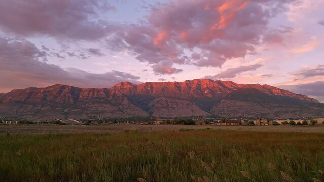 View of Timpanogos mountain during colorful sunset flying over grass field in Utah.