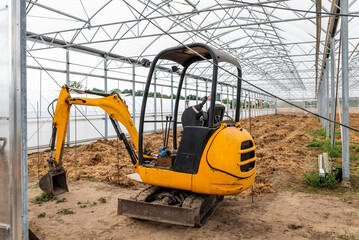 An excavator in an old greenhouse. Renovation of a greenhouse. Building greenhouses.