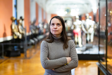 Interested young woman viewing collection of medieval knights armor in historical museum ..