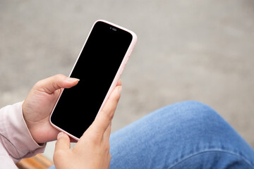 Mano de mujer revisando un celular al aire libre, pantalla de celular editable. - obrazy, fototapety, plakaty