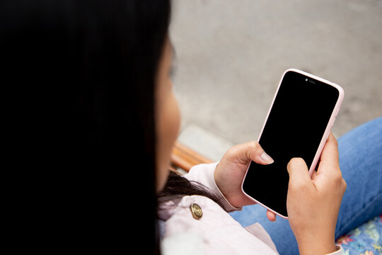 Mujer sentada al aire libre revisando un celular, pantalla de celular editable.