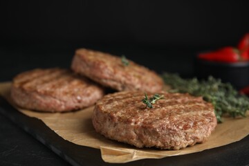 Tasty grilled hamburger patties with thyme on black table, closeup