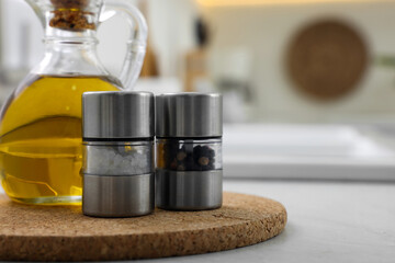 Salt and pepper mills with bottle of oil on table in kitchen. Space for text