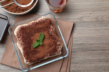 Glass bowl with delicious tiramisu cake on wooden table, flat lay. Space for text