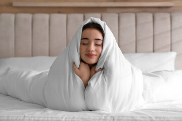 Beautiful young woman covered with warm blanket on bed at home