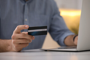 Man using laptop and credit card for online payment at table indoors, closeup