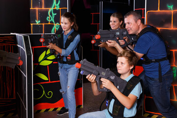 Fototapeta na wymiar Group of happy children and adults with laser guns having fun on lasertag room