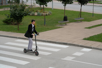 Young business man in suit driving an electric scooter to work through the city street with a cup of coffee in his hand.  © Malik Nalik