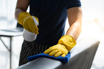 Close-up: Hands of a restaurant worker cleaning the surface of a sofa and spraying disinfectant during the coronavirus outbreak. Use a cleaner or use alcohol to disinfect the restaurant. - obrazy, fototapety, plakaty