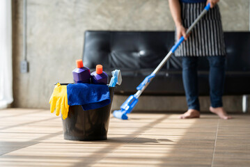 A young butler cleans the floor, mops the floor, carries a mop and a plastic bucket with brushes, gloves and detergent out of the room.