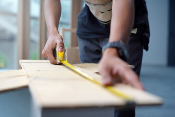 Worker measuring the length of a wooden deck with a tape measure in a workshop. Selective focus...