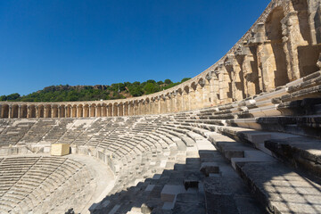 Partially restored classical Roman theater in ancient settlement of Aspendos in Antalya province of Turkey. View of stone seats of semicircle auditorium descending towards stage..