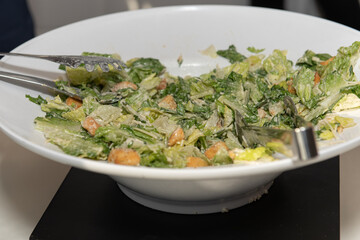 Large bowl of caesar sald has two pairs of tongs for the party guests to serve themselves food to eat