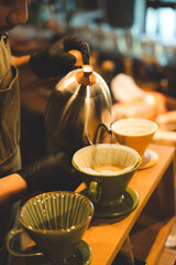 hipster barista making a drink coffee with drip or filter style by pouring hot water to brew a caffeine beverage from black bean in cafe restaurant business shop, using paper for aroma to a cup or mug