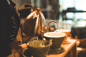 hipster barista making a drink coffee with drip or filter style by pouring hot water to brew a caffeine beverage from black bean in cafe restaurant business shop, using paper for aroma to a cup or mug