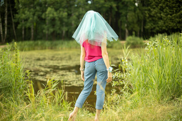 Girl in park. Girl in summer on shore of pond. Blue cape on head. Transparent veil on hair.