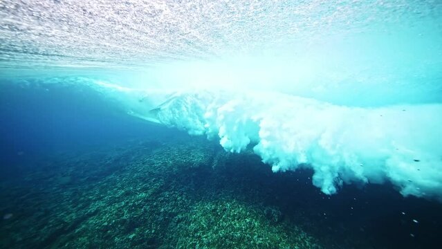 Underwater shot of male surfer silhouette riding barrel of a perfect blue ocean wave. Teahupoo famous action sports destination in Tahiti. travel in French Polynesia. 4k slow motion. 