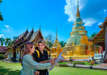 Young Asian travelers looking and studying site map of the beautiful Thai Buddhist temple, Wat...