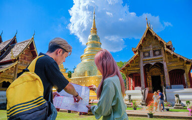 Young Asian travelers looking and studying site map of the beautiful Thai Buddhist temple, Wat...