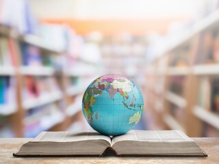 Old globe lying on an open book against the background of bookshelves in a library. Science,...
