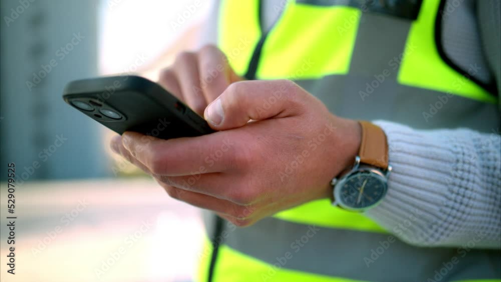 Poster construction worker texting on a phone, standing outdoors at a building site. closeup of an architec