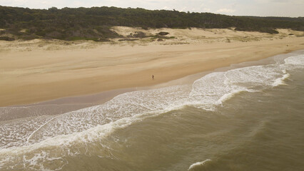 Aerial drone shot of isolated person walking on beach at sunset, Playa Grande in Uruguay