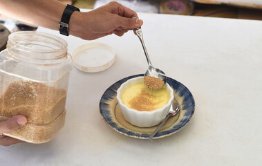 Process of sprinkling brown sugar on the Creme brulee on white background