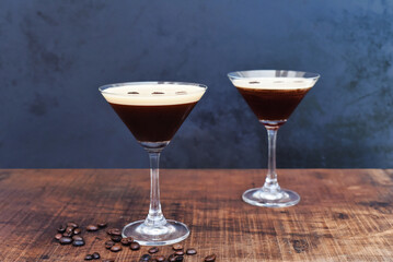 Glasses of espresso martini with coffee beans on wooden table and black background