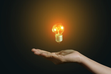 A person's hand with a bright light bulb floating above his hand on a dark background - copy space