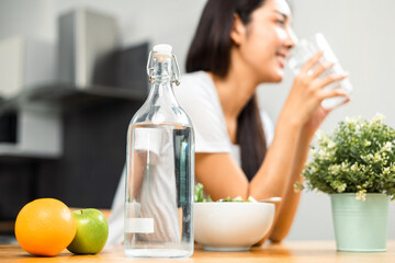 Young female drinking water in glass for refreshing for diet and wellness on table. Beautiful woman happily drink fresh water before breakfast in kitchen in the morning. Healthy food concept.