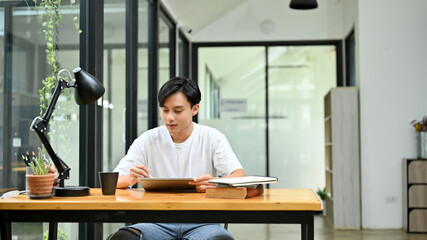 Handsome Asian male freelance graphic designer or office worker using digital tablet.