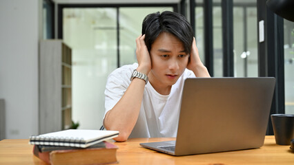 Stressed and depressed Asian male office worker or college student looking at laptop screen