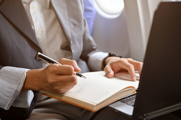 A businessman taking notes on his notebook, using laptop during the flight to a business trip