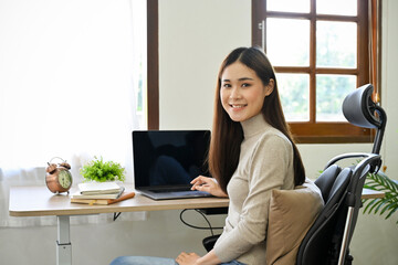 Gorgeous Asian female businesswoman sits at her desk, looking and smiling to camera.